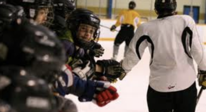 Back of hockey player skating while tapping teammates gloves on the bench.