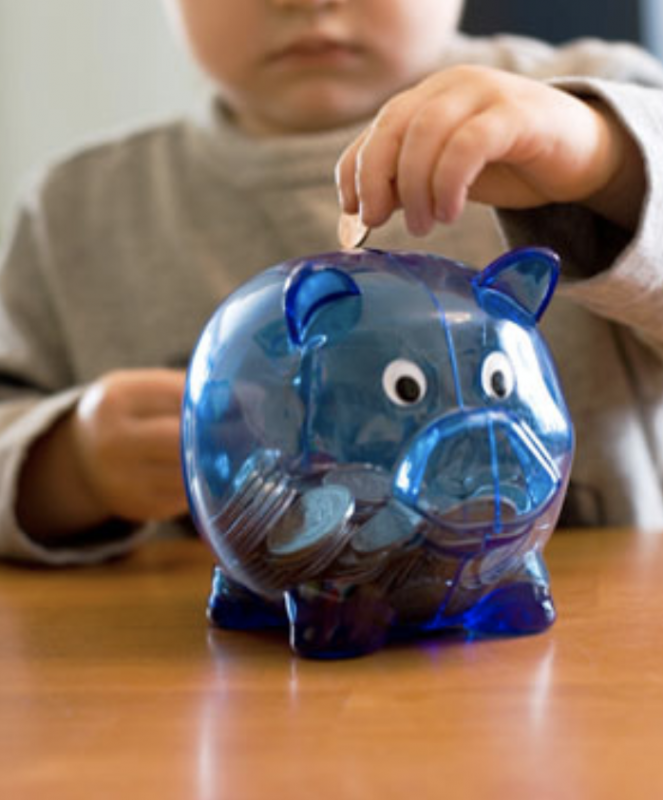Young boy putting coin into a piggy bank