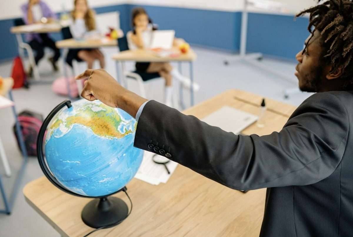 Teacher pointing to globe in front of class