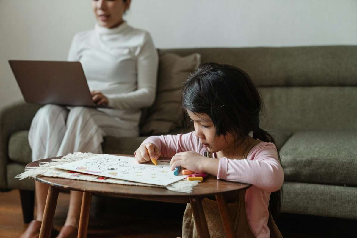 mother on laptop with child colouring