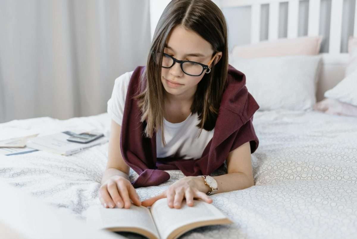 Girl with glasses reading book on bed