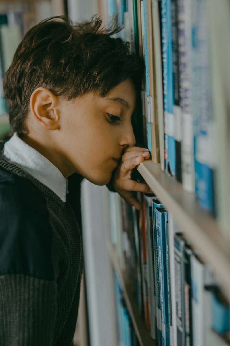 sad tween boy leaning on book shelf