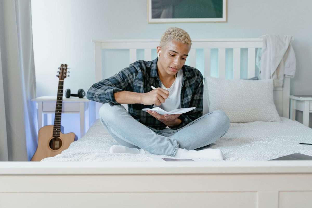 A Young Man Doing his Homework while Sitting on a Bed
