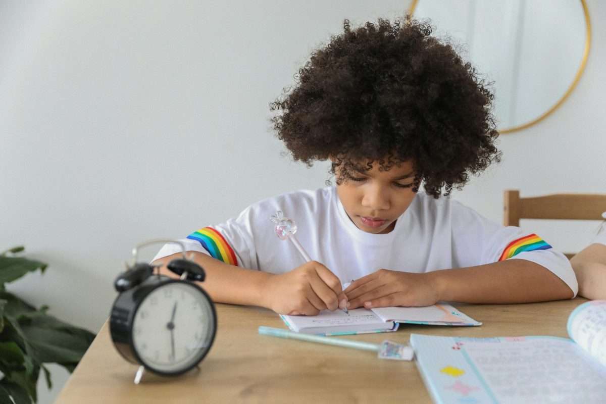 Focused black schoolgirl doing homework at table in house