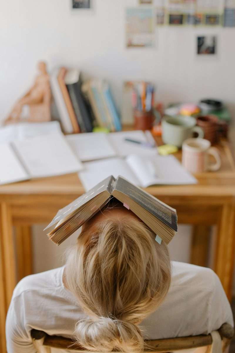 female student with book covering her face at a desk