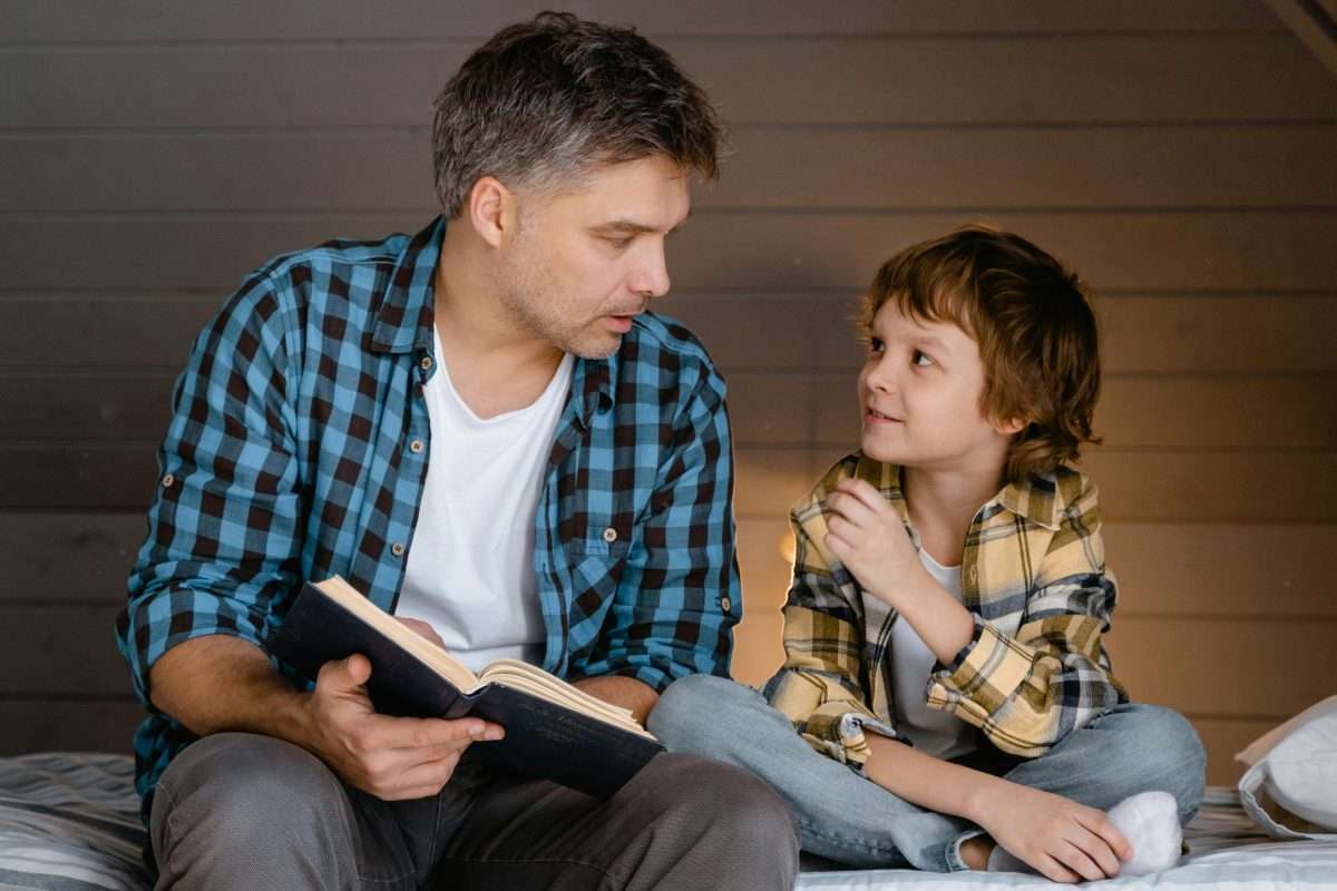 man and young boy reading on a bed