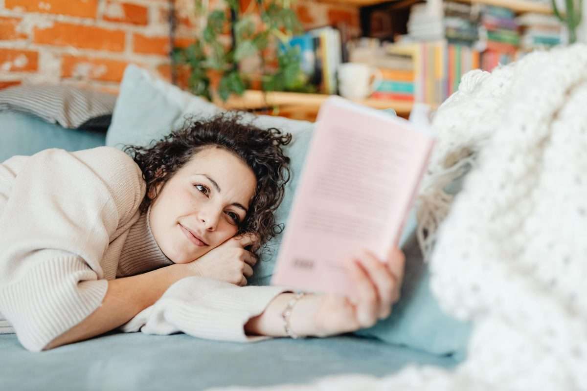 Smiling Woman Lying on a Couch and Reading a Book